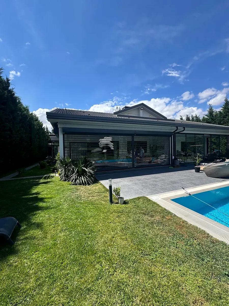 Vista desde el jardín: terraza con sistema de persiana transparente y piscina